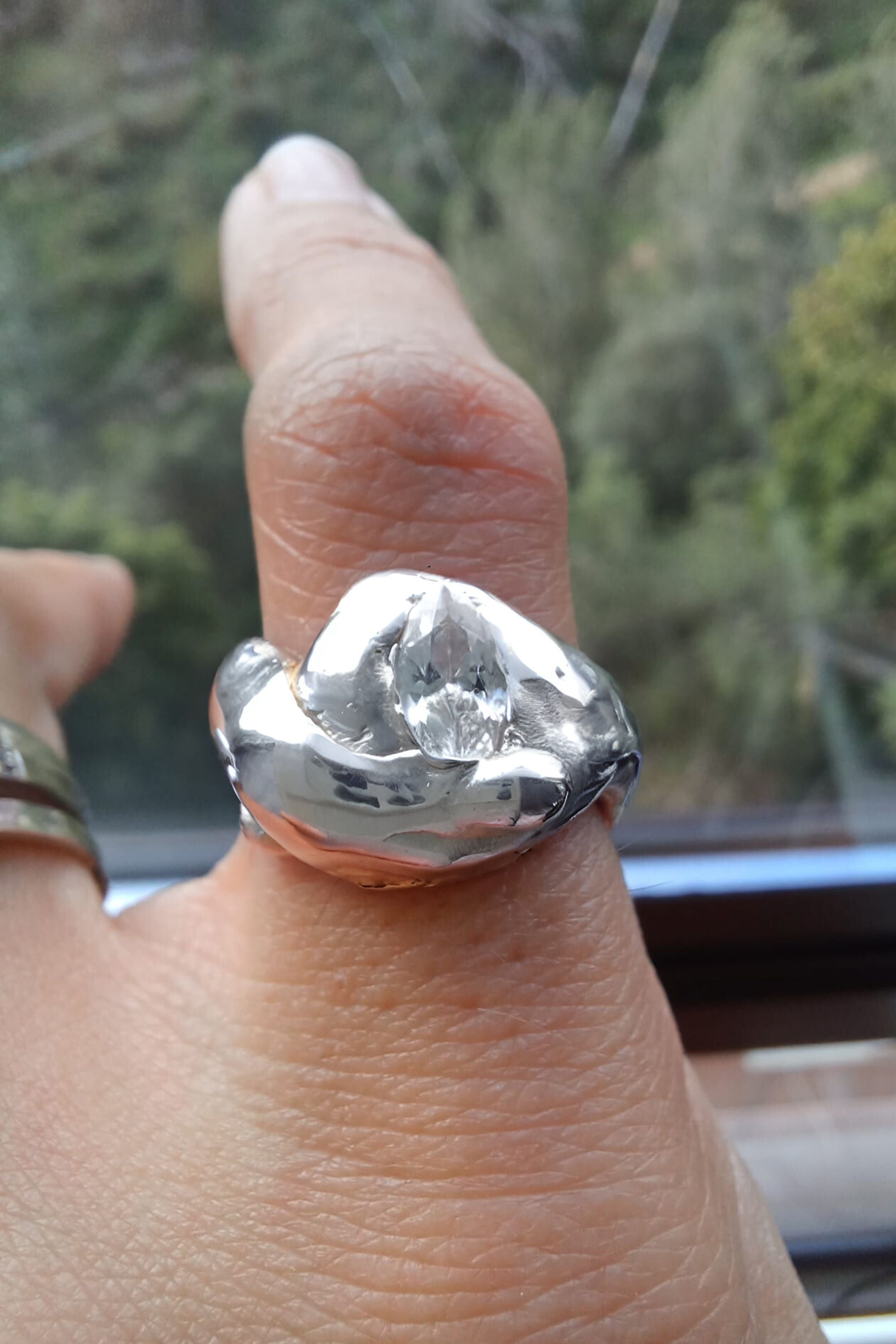 Silver ring with a large diamond on a finger, blurred green background