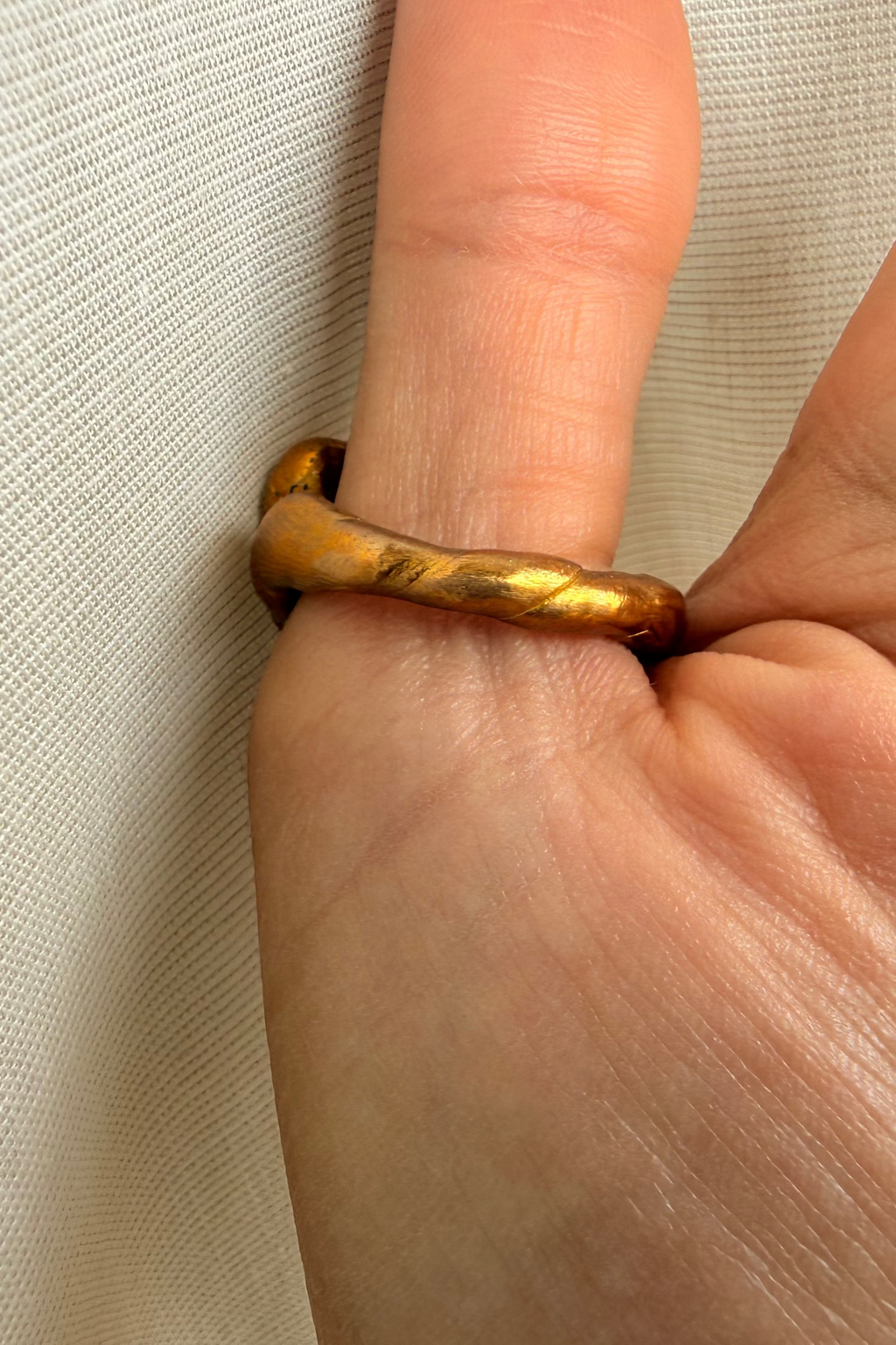 Close-up of a hand wearing a gold ring on a neutral background