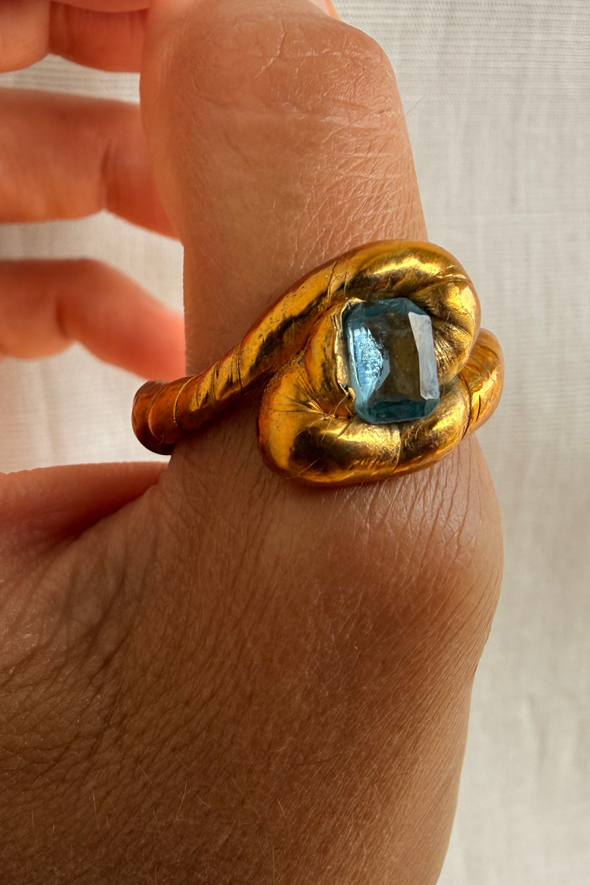 Gold ring with a blue gemstone on a person's finger against a neutral background