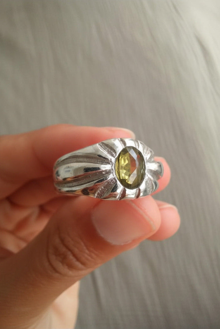 Silver ring with a yellow gemstone held in a hand against a neutral background