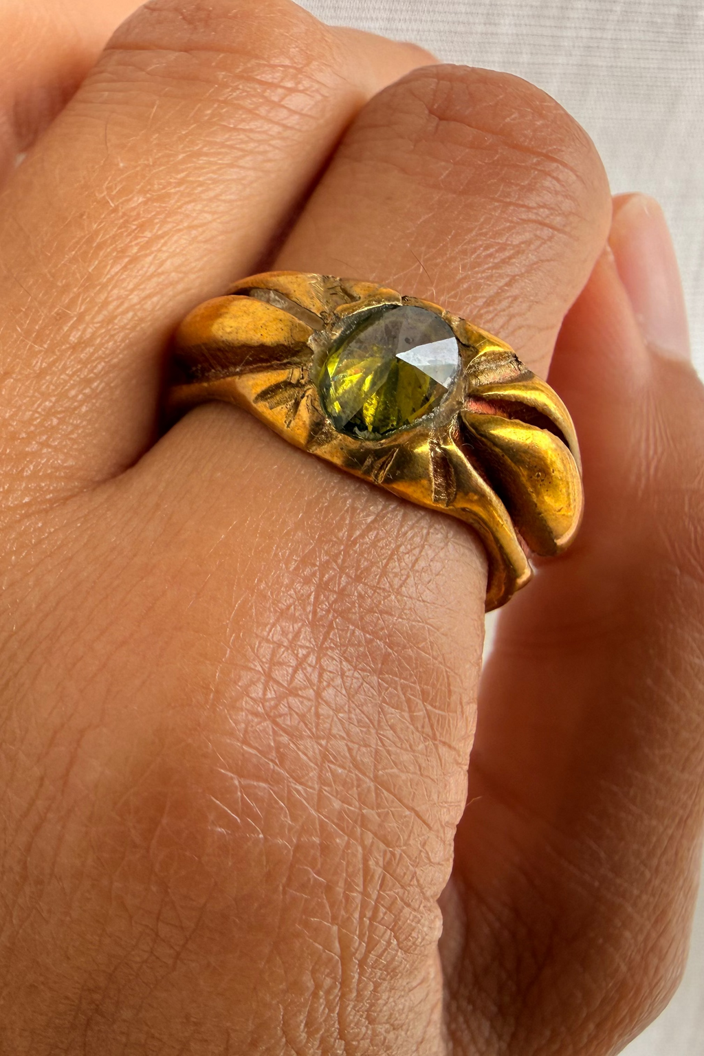 Gold ring with a green gemstone on a hand against a neutral background