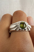 Silver ring with a green gemstone on a person's finger against a white background