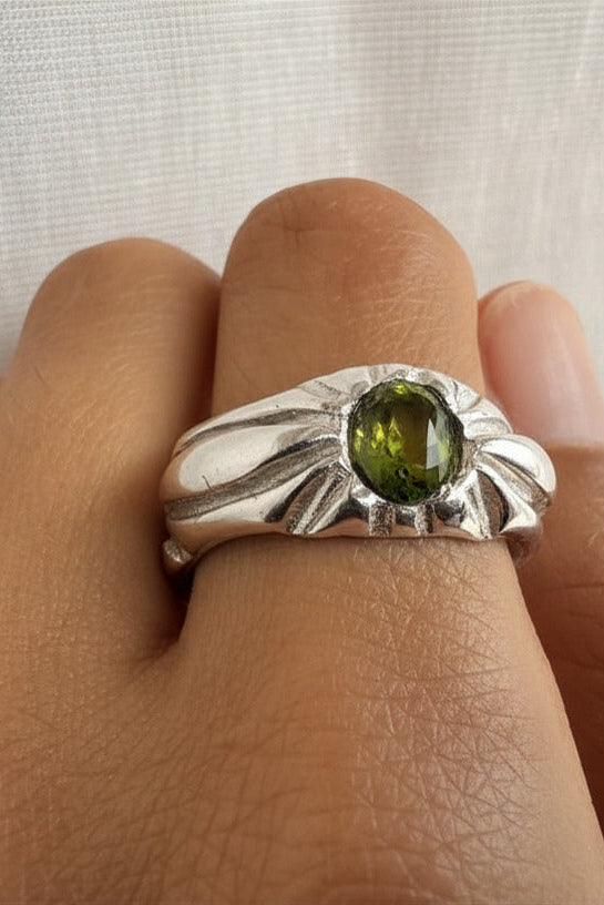 Silver ring with a green gemstone on a person's finger against a white background