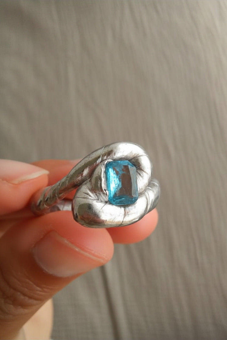 Silver ring with a blue gemstone held in a hand against a neutral background